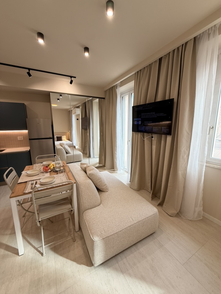 Monolocale Blu: living area with sofa, dining table, wall-mounted TV and mirrored wardrobe
