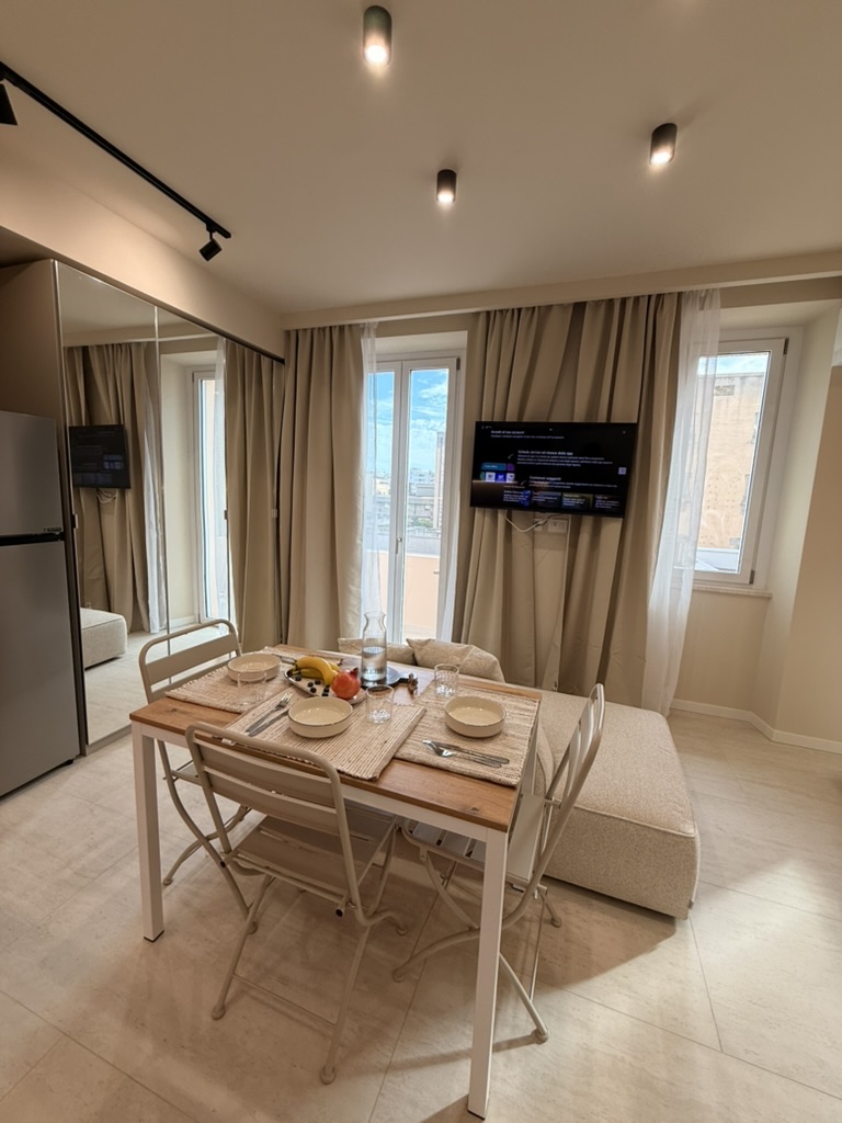 Monolocale Blu: dining table set for a meal, sofa and windows with floor-length curtains