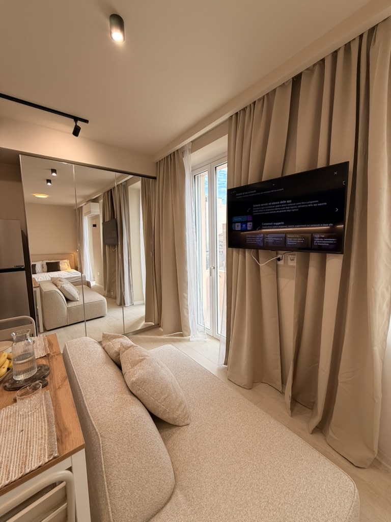 Monolocale Blu: sofa facing the 43-inch wall-mounted TV, with blackout curtains